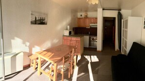 A compact living space with a dining table and chairs, a kitchenette, a black sofa, and a small kitchen area. - 50m from resort center, 5th floor, balcony, tv, ski locker, 28m², Serre Chevalier (La Salle-les-Alpes)