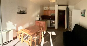 A compact living space with a dining table and chairs, a kitchenette, a black sofa, and a small kitchen area.