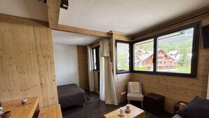 En inredning med träpanel, en soffa, ett litet bord och en stol. Det finns fönster med utsikt över byggnaderna utanför.