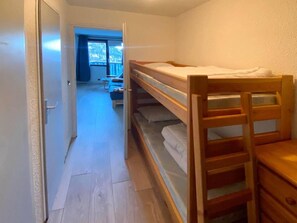 A room with a bunk bed, a wooden desk, and a door leading to another room.