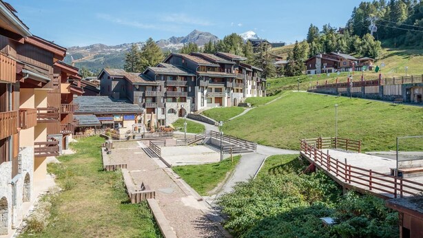 A mountain resort with chalet-style buildings, a ski lift, and a clear view of the surrounding mountains.