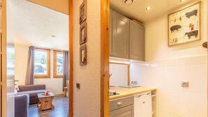 A compact living space with a kitchenette, a dining area with a sofa and a small table, and a view through an open door to a balcony.