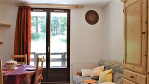 A room with a dining table set for two, a sofa with cushions, a wooden cabinet, and a sliding glass door leading outside. - 50m from ski slopes, Ground floor, balcony, tv, ski locker, 28m², Risoul (Risoul)