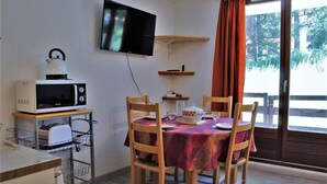 A dining area with a table set for four, a microwave, a television, and a window with curtains. - 50m from ski slopes, Ground floor, balcony, tv, ski locker, 28m², Risoul (Risoul)