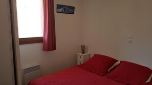 A bedroom with a bed, a nightstand, a lamp, a heater, a window with curtains, and a picture on the wall. - 50m from ski slopes, 3rd floor, swimming pool, 37m², Valloire (Valloire)