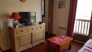 A room with a wooden cabinet, a television, a table with a red tablecloth, and a window with a view of a wooden deck. - 50m from ski slopes, 3rd floor, swimming pool, 37m², Valloire (Valloire)