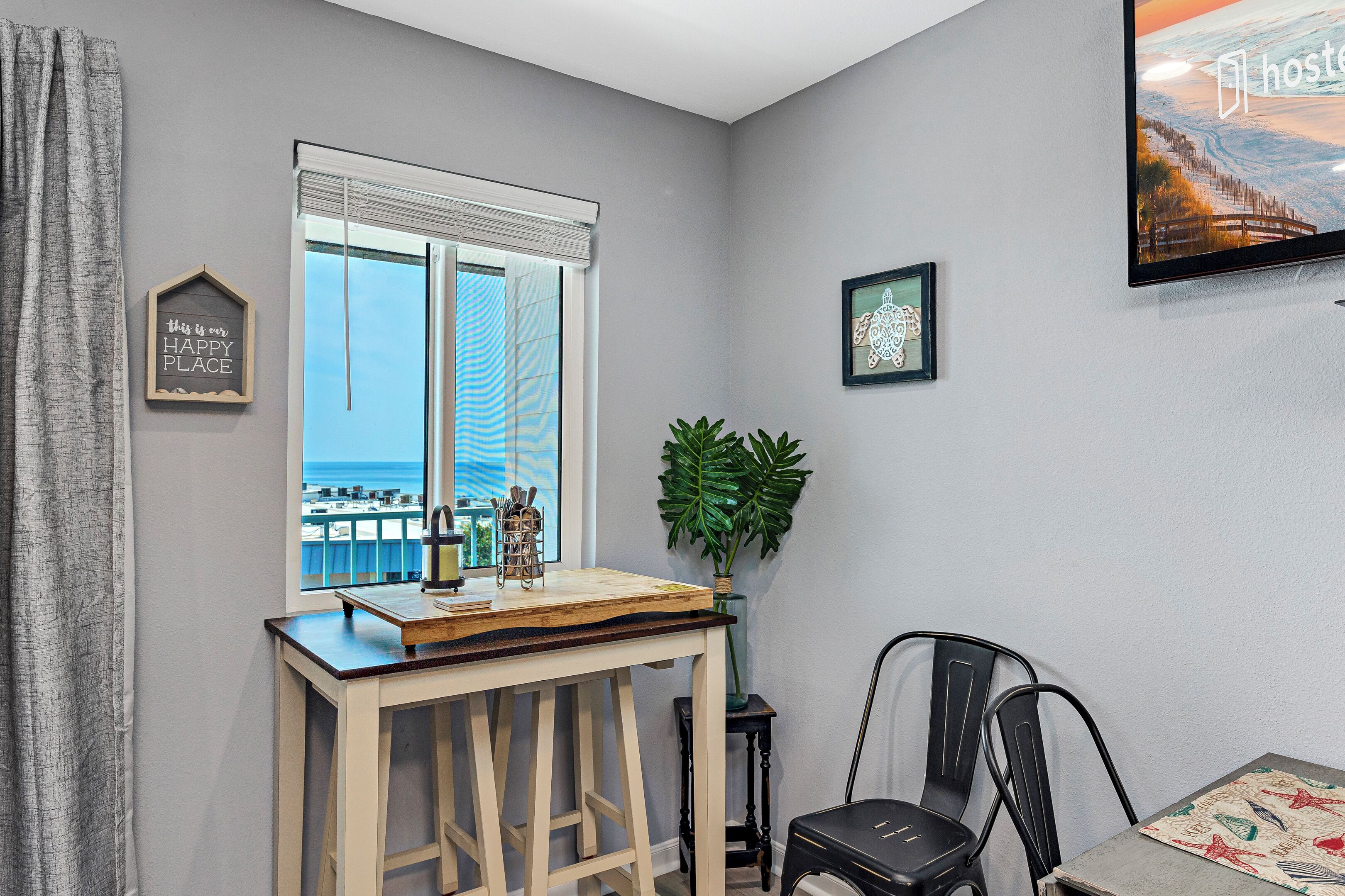 Una habitación con vista al océano, una mesa de madera con una planta y un cuadro en la pared.