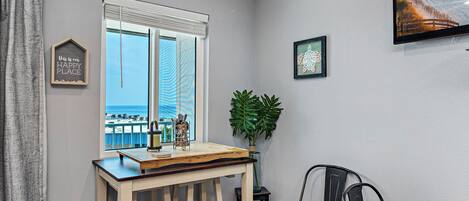 Una habitación con vista al océano, una mesa de madera con una planta y un cuadro en la pared.