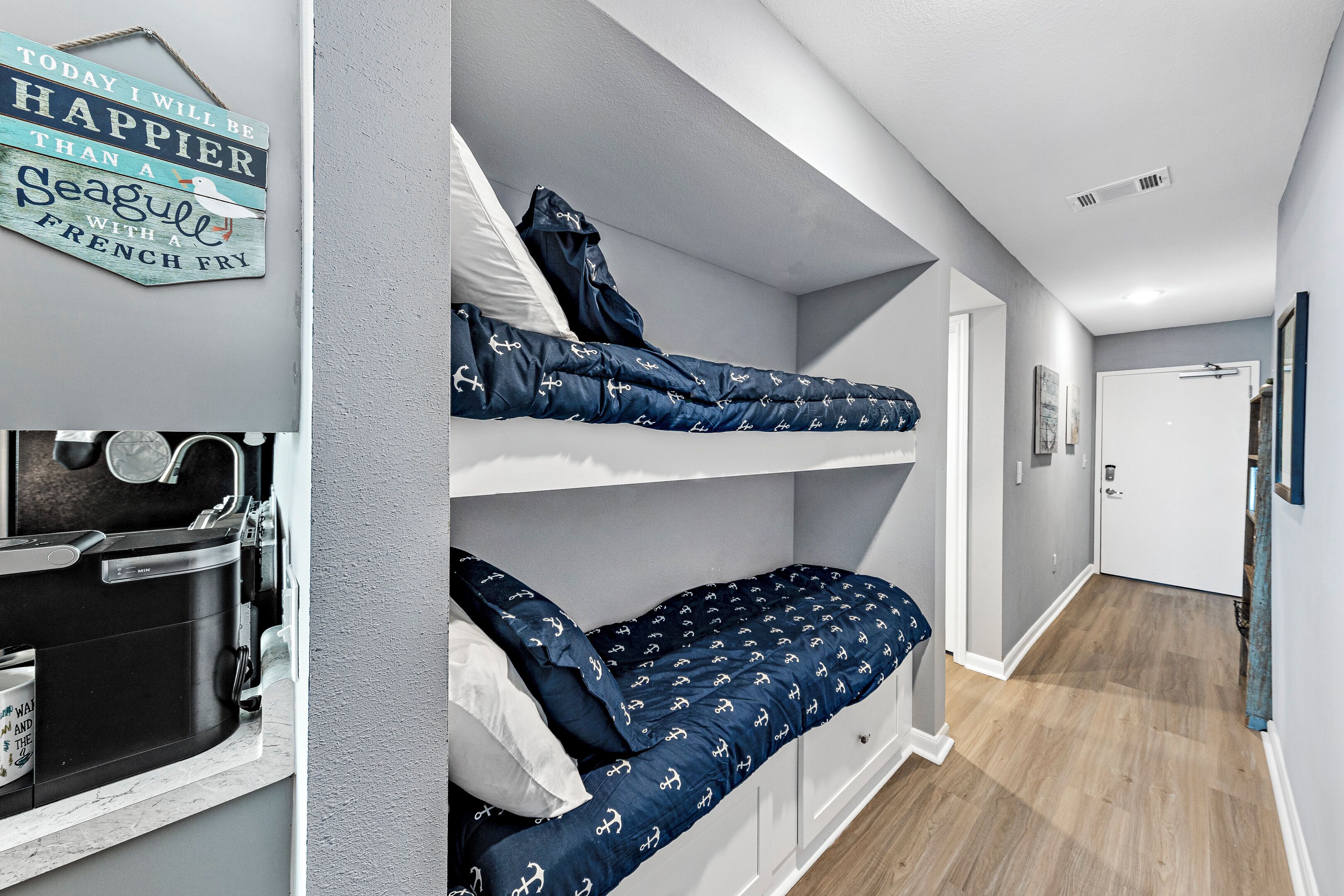 A compact room with bunk beds, a small kitchenette, and a hallway leading to a door.