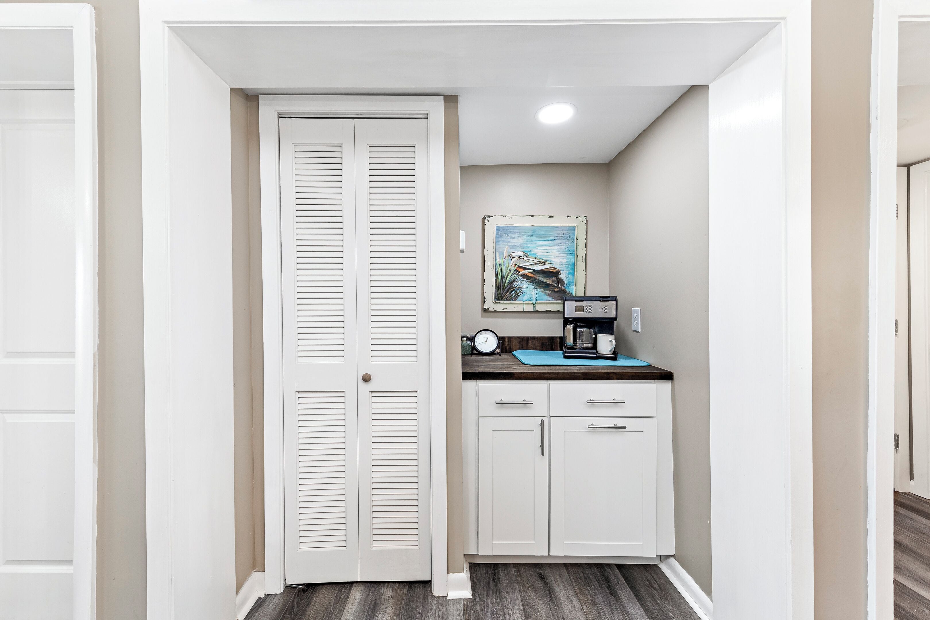 A compact kitchen with white cabinets, a coffee maker, and a clock on the wall.