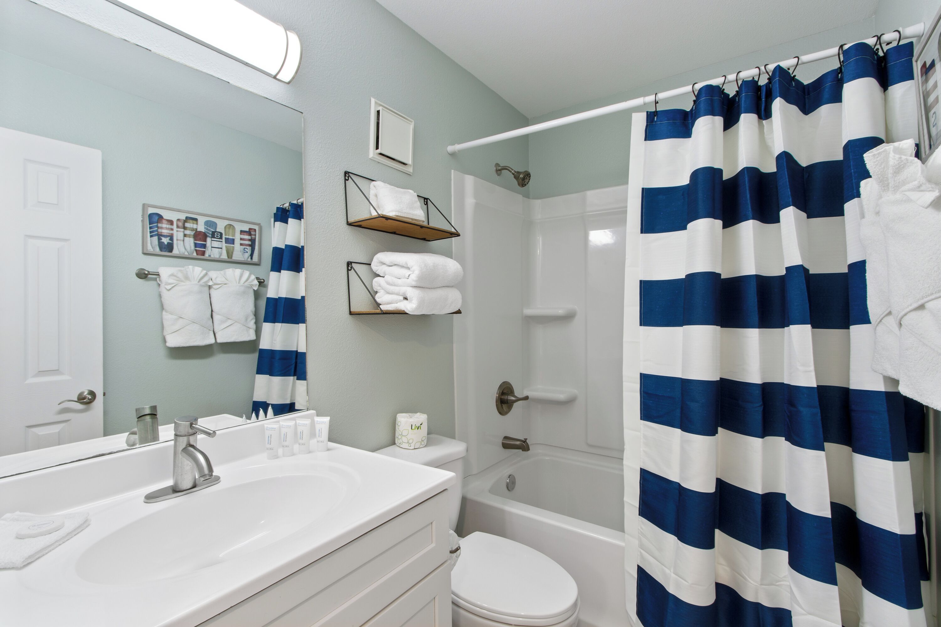 A bathroom with a white sink, a toilet, a shower curtain, and a towel rack with folded towels.