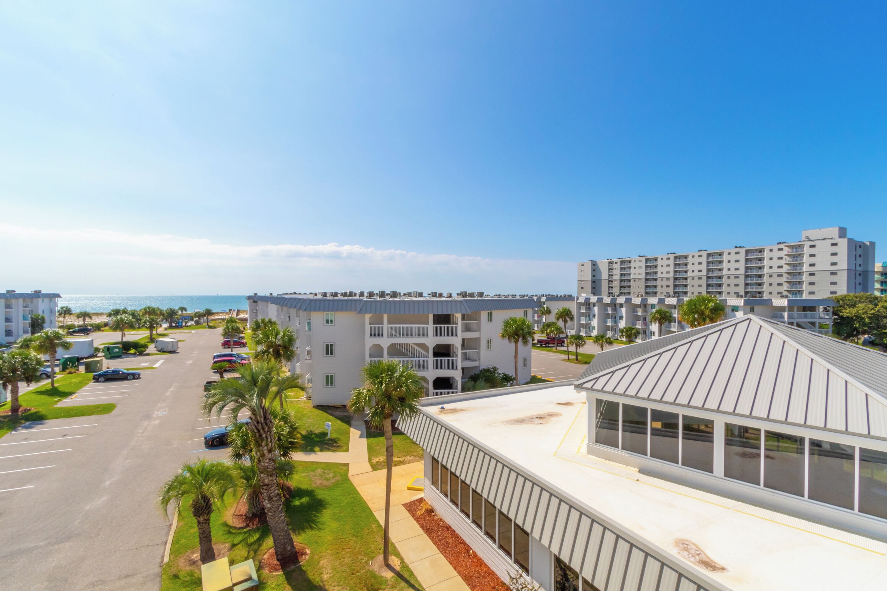A modern hotel with a parking lot, palm trees, and a view of the ocean.