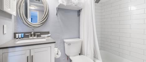 A bathroom with a white toilet, sink, and bathtub. There is a shower curtain and a mirror above the sink.