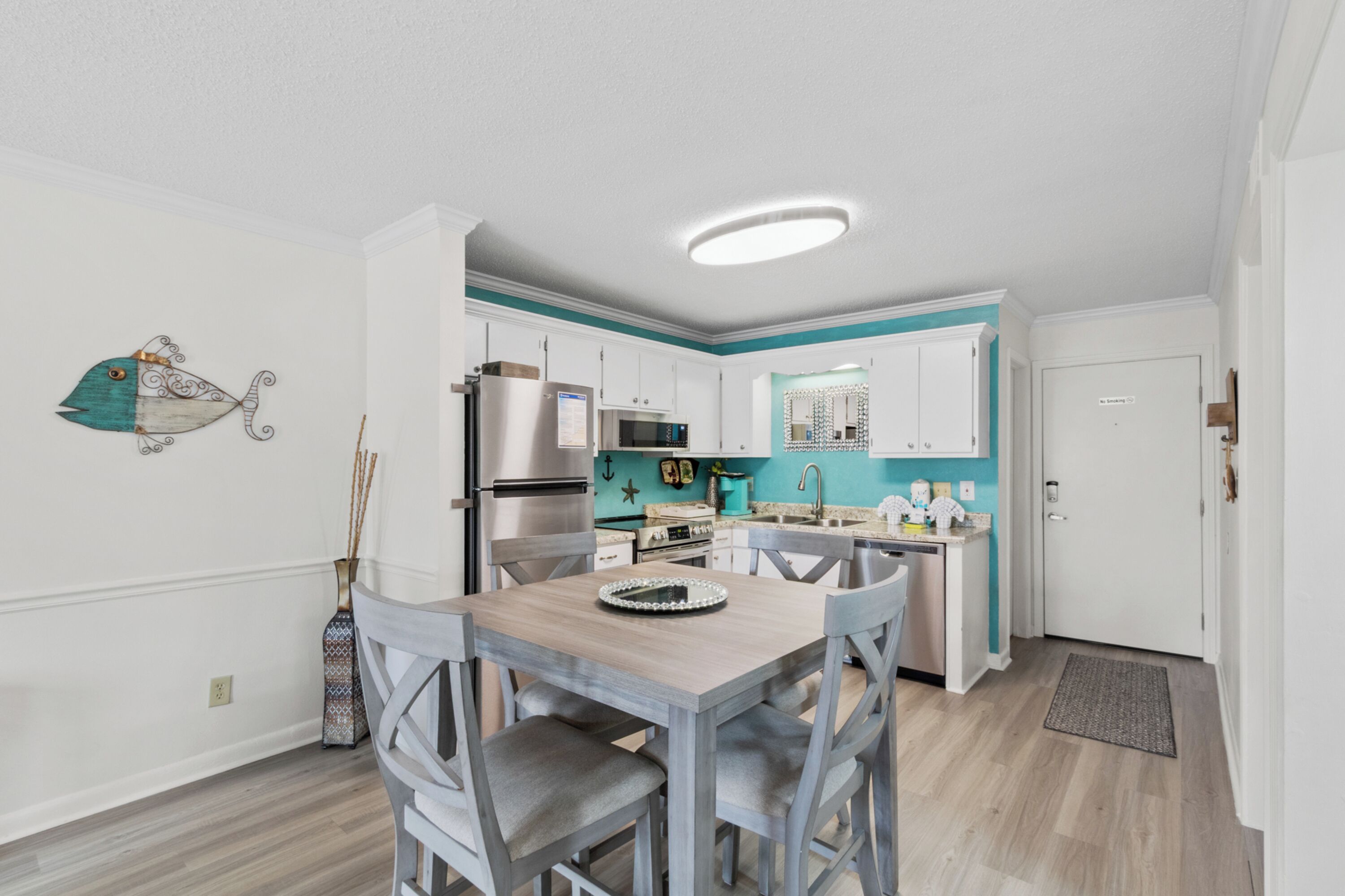 Una cocina moderna con armarios blancos, una mesa de comedor de madera y una pared de acento color turquesa.