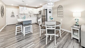 Una cocina moderna con armarios blancos, un refrigerador de acero inoxidable y un comedor con una mesa redonda y sillas.