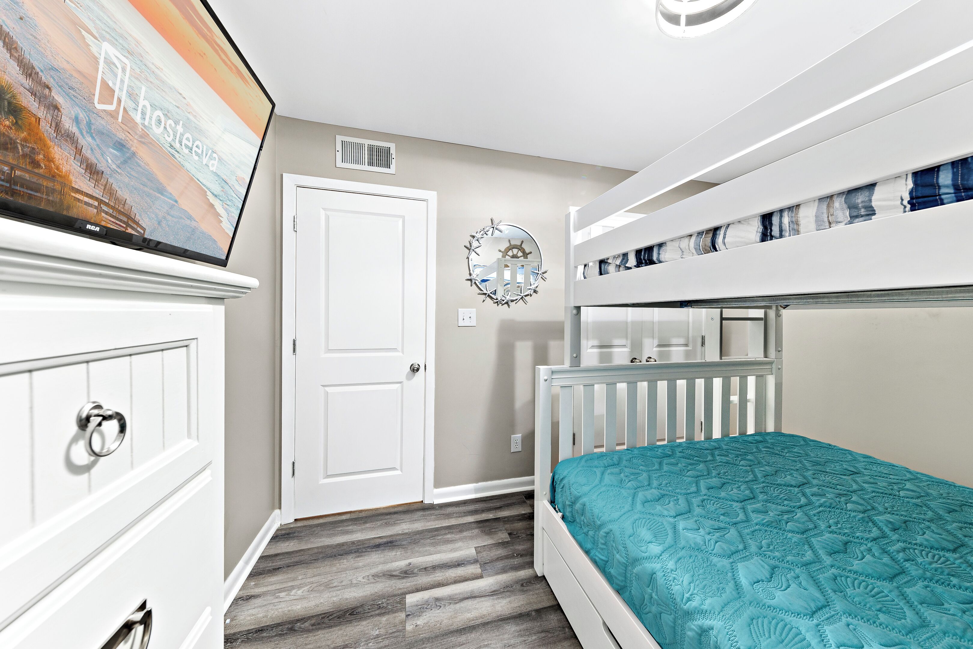 A bedroom with a bunk bed, a dresser, a television, and a wall clock.