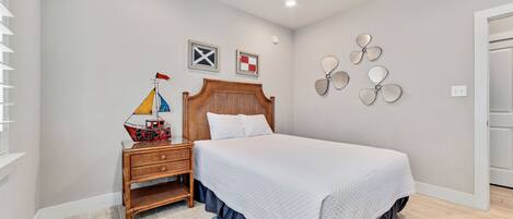 Een slaapkamer met een bed, nachtkastje, plafondventilator en decoratieve wandversiering.