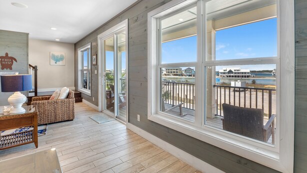 A spacious room with large windows, a balcony with a view of the beach, and a cozy seating area with a table and chairs. - Turtle Tracks | Outdoor Pool | Steps from Beach | Waterfront | My Beach Getaways (Gulf Shores)