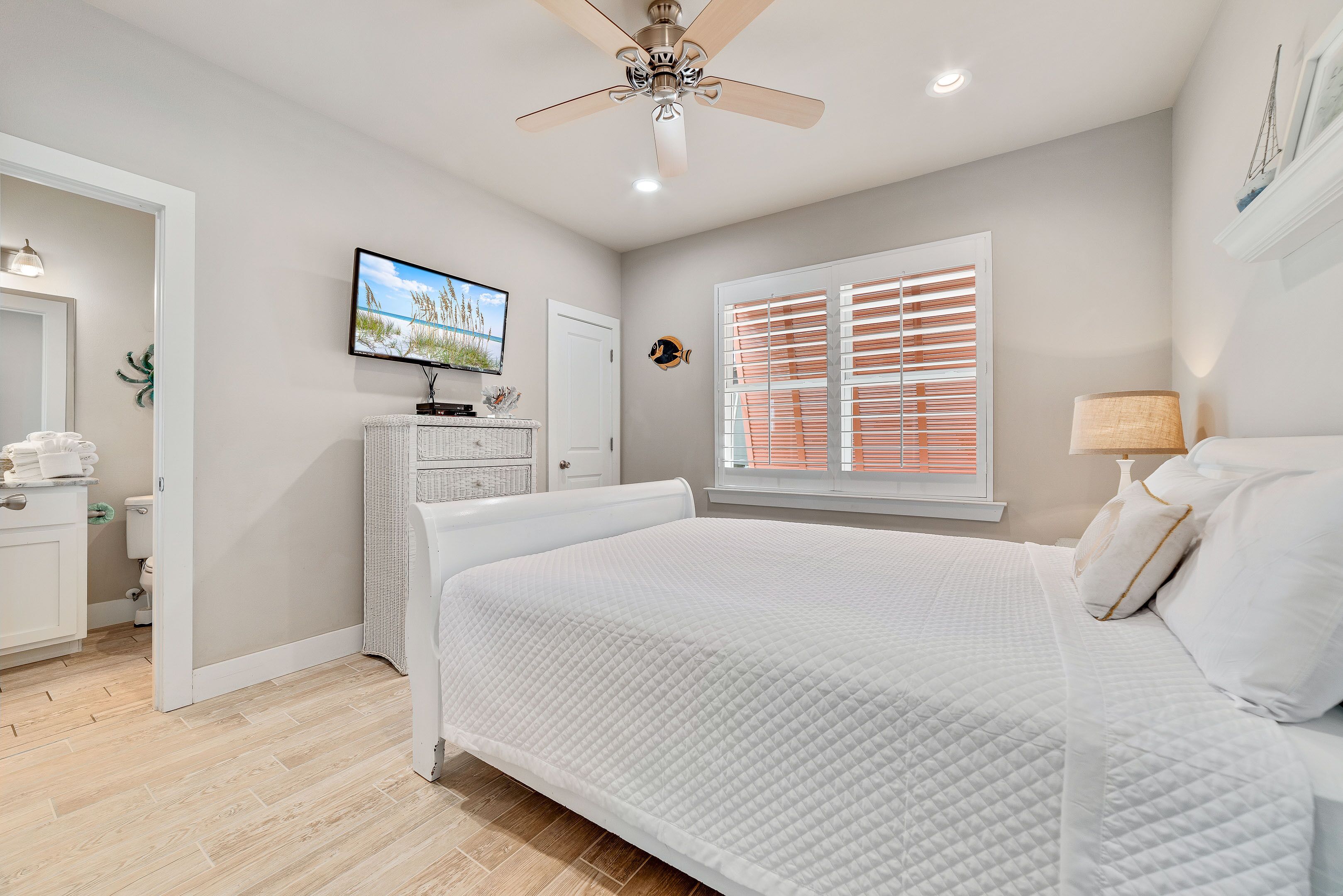 Une chambre à coucher comprenant un lit, un ventilateur de plafond, un téléviseur, une fenêtre avec des stores et une table de chevet.
