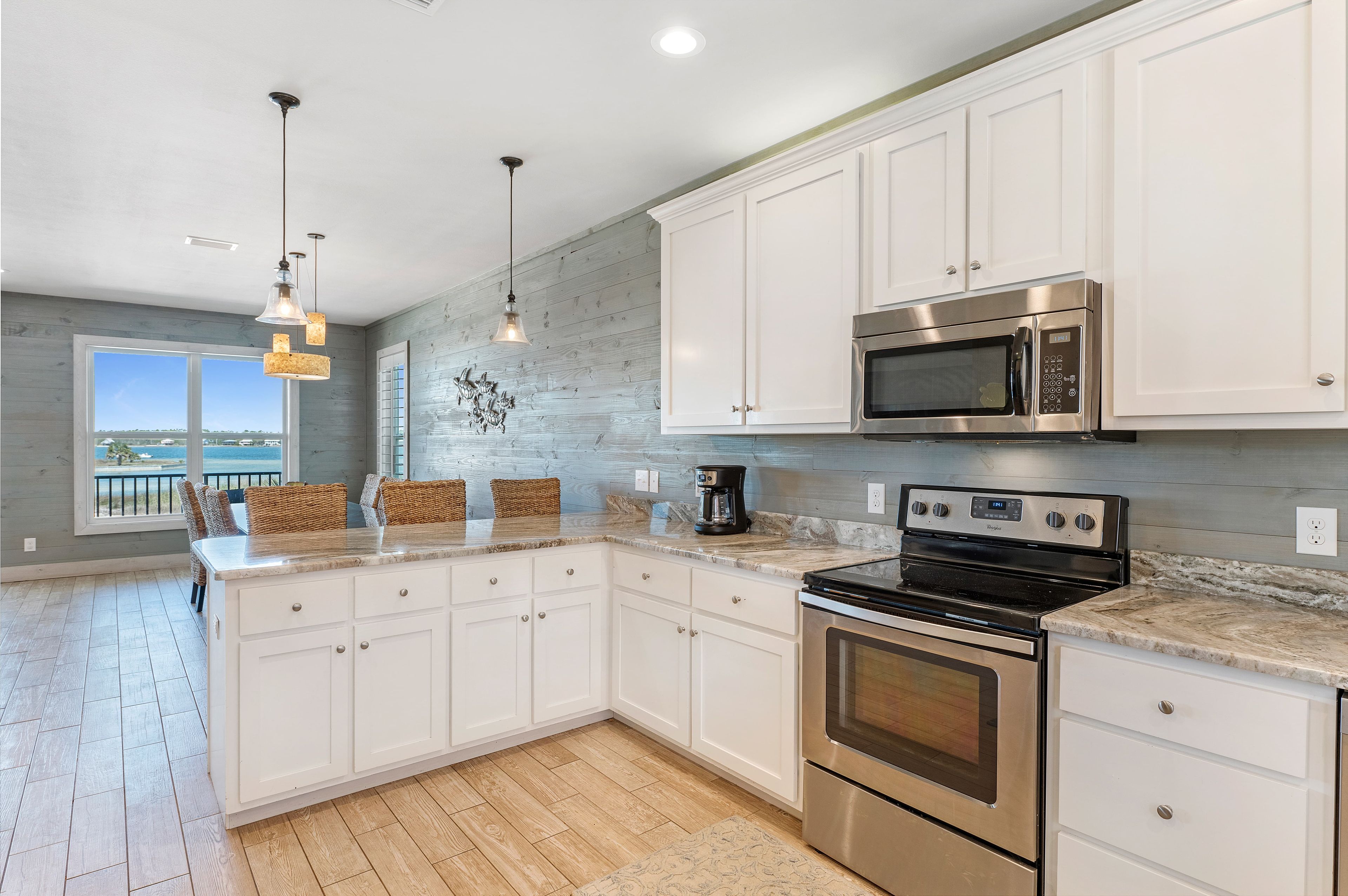 A modern kitchen with white cabinets, stainless steel appliances, a large island with seating, and a view to the outside.