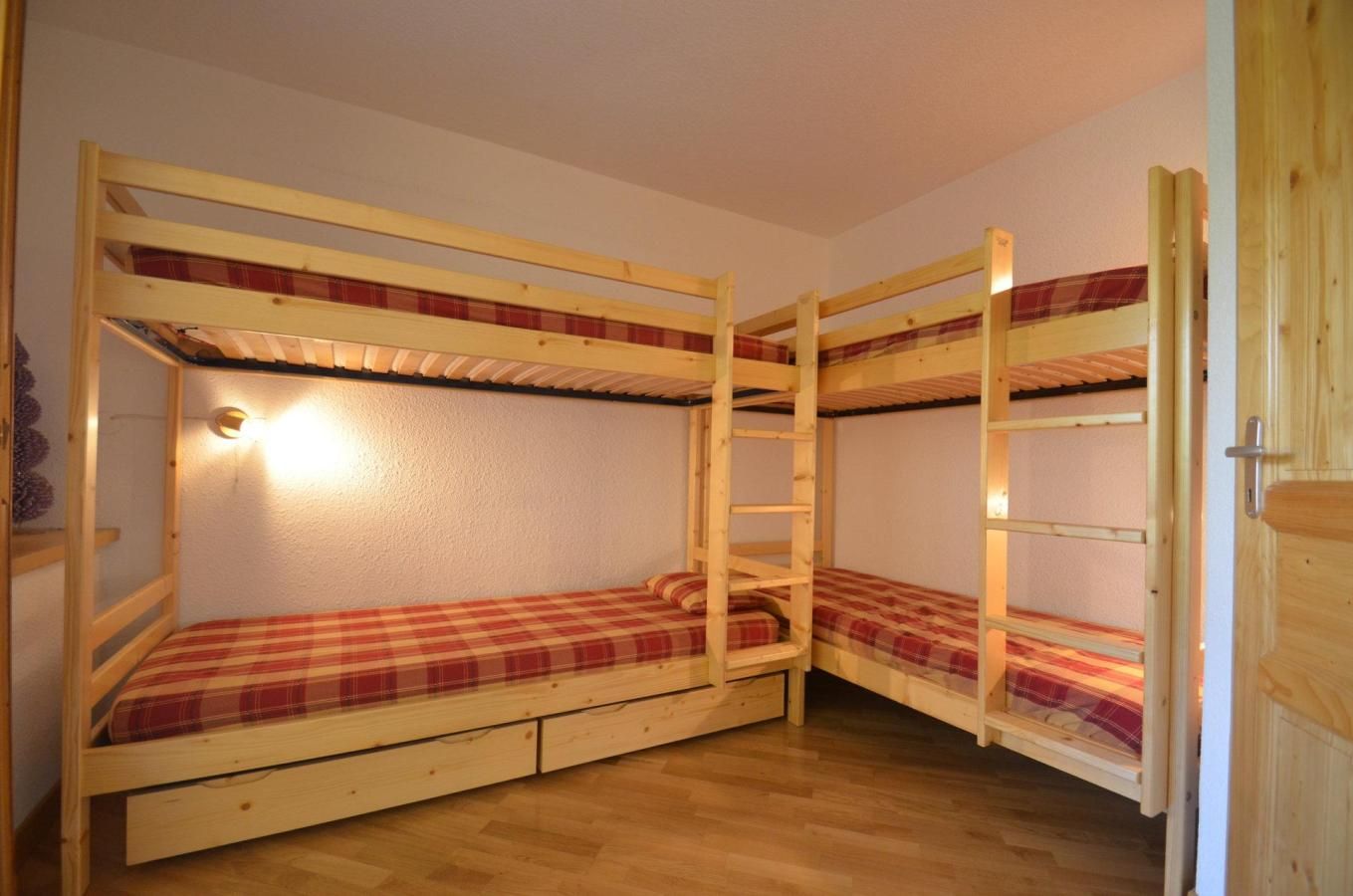 A bunk bed room with wooden frames, a ladder, and a wall-mounted light fixture.