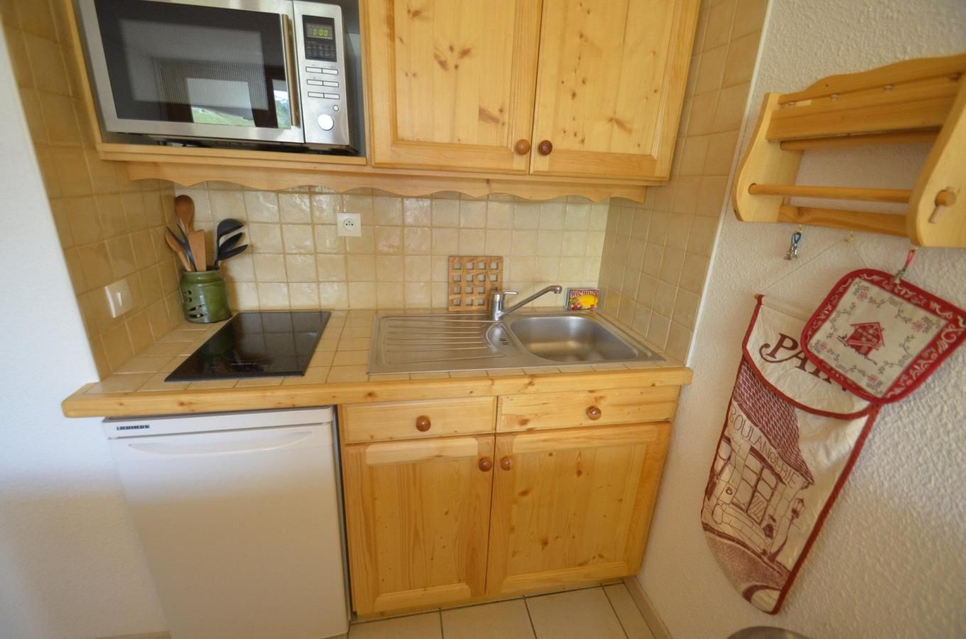 A compact kitchen with wooden cabinets, a microwave, a sink, and a dishwasher.