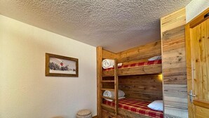 A room with a bunk bed, a small stool, a framed picture on the wall, and a wooden door. - 10m from ski slopes, 7th floor, balcony, tv, 28m², Les Menuires (Les Menuires)