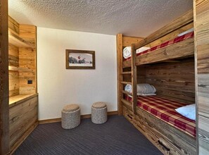 A cozy room with a bunk bed, two stone stools, a framed picture on the wall, and wooden paneling. - 10m from ski slopes, 7th floor, balcony, tv, 28m², Les Menuires (Les Menuires)