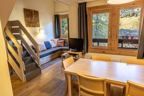 Ett mysigt rum med en trätrappa, en soffa med kuddar, en tv och ett matbord med stolar.