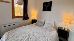A neatly arranged bedroom with a bed, two bedside tables with lamps, a window with curtains, and a wall-mounted artwork. - 100m from ski slopes, 3rd floor, view mountain, balcony, tv, ski locker, 33m², Montchavin La Plagne (Bellentre)