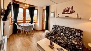 A cozy living room with a patterned sofa, a dining table with chairs, and a kitchen area with a window. - 100m from ski slopes, 3rd floor, view mountain, balcony, tv, ski locker, 33m², Montchavin La Plagne (Bellentre)