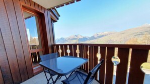 A balcony with a glass table and chairs, wooden railings, and a view of distant mountains. - 100m from ski slopes, 3rd floor, view mountain, balcony, tv, ski locker, 33m², Montchavin La Plagne (Bellentre)