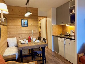 A cozy room with a wooden dining table set for two, a sofa, and a kitchen area with cabinets and appliances.
