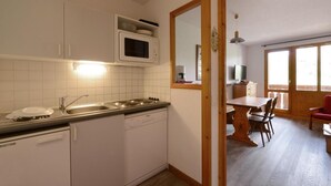 Eine kompakte Küche mit Geschirrspüler, Herd und Mikrowelle. Ein Essbereich mit Tisch und Stühlen ist vorhanden.