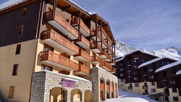 Ein mehrstöckiges Hotel mit Balkonen, Steinarchitektur und einem verschneiten Berg im Hintergrund.