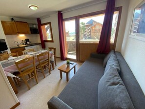 A compact living space with a dining area, a sofa, and a view of a wooden building through a large window.