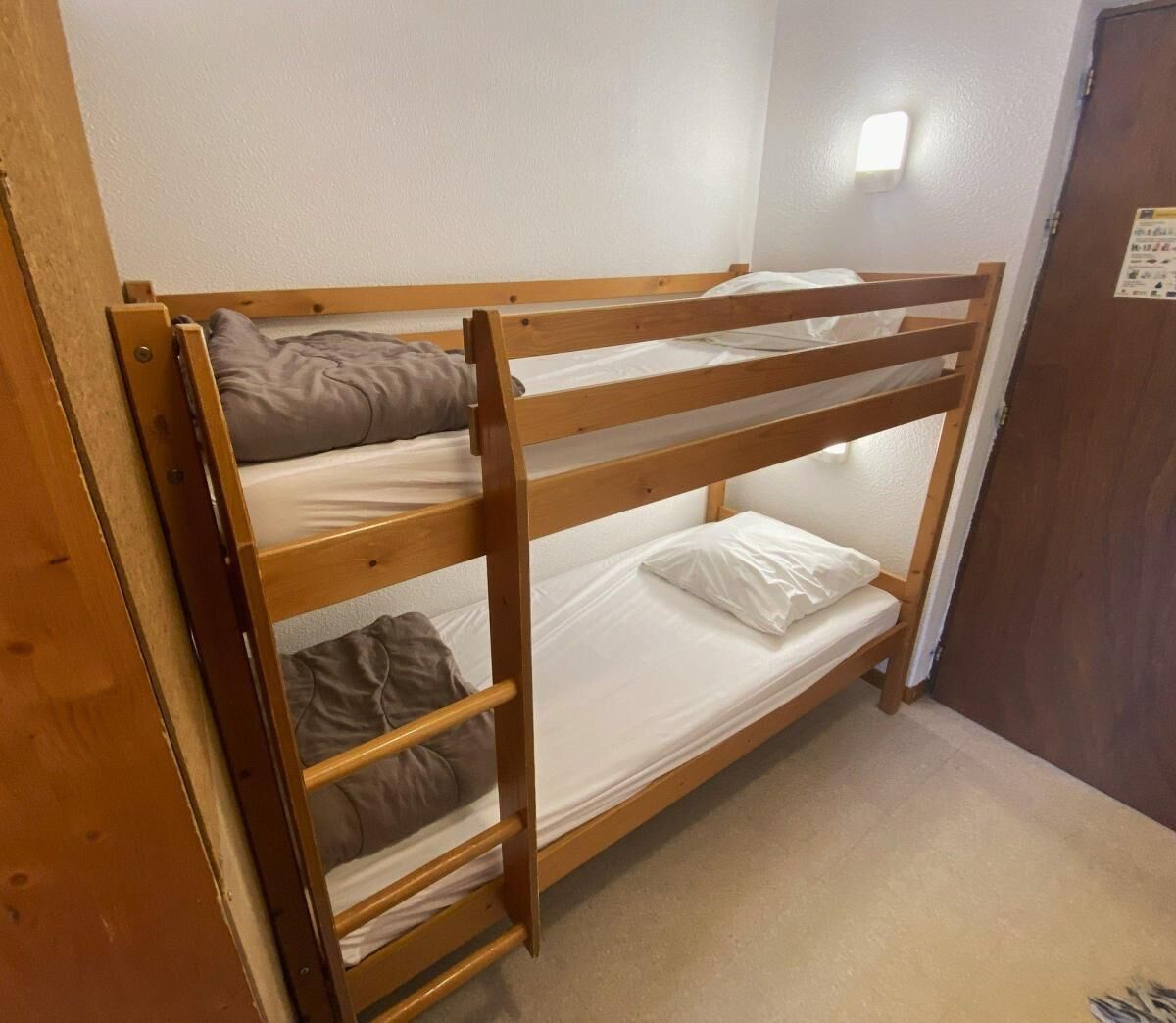 Una cama litera con escalera, una pared blanca y una puerta con un cartel.