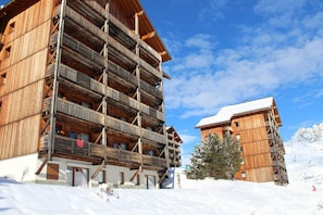Eine Holzhütte mit mehreren Balkonen und einem mit Schnee bedeckten Dach, eingebettet in eine verschneite Landschaft.