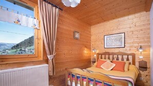 Ein gemütlicher Holzraum mit einem Bett, einem Fenster mit Vorhängen, einer Heizung und einer gerahmten Karte an der Wand.