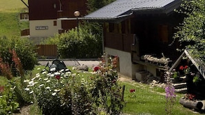 A chalet-style building with a sloped roof, surrounded by a lush garden with various flowers and plants. - 300m from ski slopes, parking, tv, 44m², Arêches-Beaufort (Beaufort)