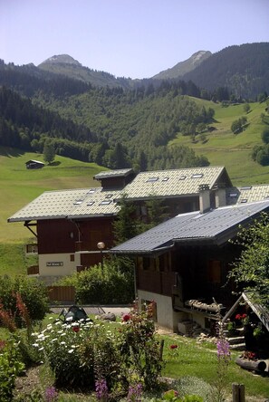 A chalet-style building with a sloped roof, surrounded by a lush garden with various flowers and plants. - 300m from ski slopes, parking, tv, 44m², Arêches-Beaufort (Beaufort)