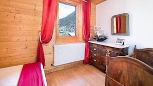 Ein Zimmer mit Holzwänden, einem Bett, einem Schminktisch, einem Spiegel und einem Fenster mit roten Vorhängen.