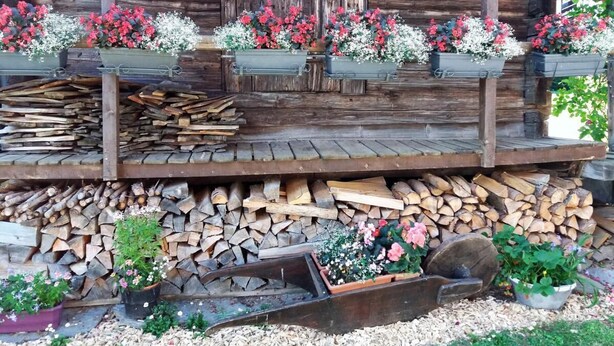 Eine rustikale Holzhütte mit Blumenkästen am Balkon und einem Holzstapel im Hintergrund.