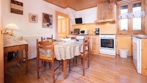 Eine gemütliche Küche mit Holzausstattung, einem Esstisch mit Stühlen, einer Mikrowelle, einem Backofen und einem Spülbecken.