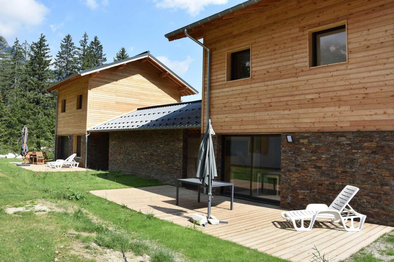 Une maison moderne en bois dotée d’un patio, d’un espace salon extérieur et offrant une vue sur la forêt environnante.