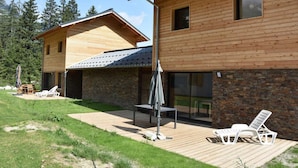 Une maison moderne en bois dotée d’un patio, d’un espace salon extérieur et offrant une vue sur la forêt environnante.