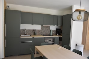 A modern kitchen with grey cabinets, a wooden countertop, a built-in oven, and a hanging light fixture.
