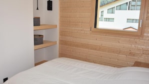 Une chambre avec un mur en lambris de bois, une fenêtre donnant sur un immeuble et des étagères intégrées avec des paniers de rangement.