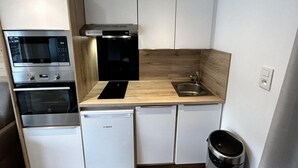 A compact kitchen with built-in appliances including a microwave, oven, and dishwasher, a sink, and wooden cabinetry. - 10m from ski slopes, 2nd floor, view mountain, tv, ski locker, 27m², Les Menuires (Les Menuires)