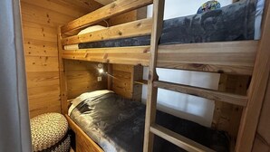 A bunk bed room with wooden walls and a small round stool. - 10m from ski slopes, 2nd floor, view mountain, tv, ski locker, 27m², Les Menuires (Les Menuires)